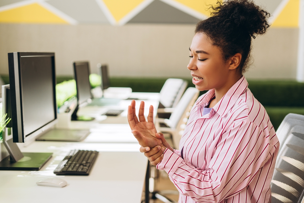 Young female office worker massages her wrist, experiencing pain and discomfort after prolonged computer work