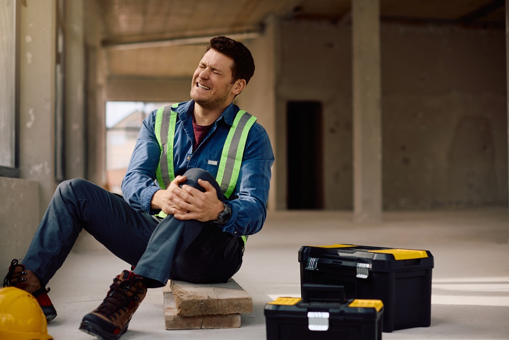 Construction site worker feeling pain in his leg after an injury at work.