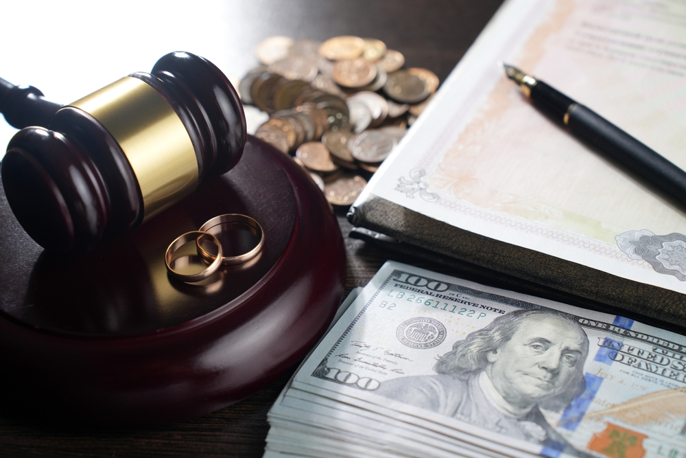 wedding rings on judge gavel with money, coins, fountain pen and legal document.