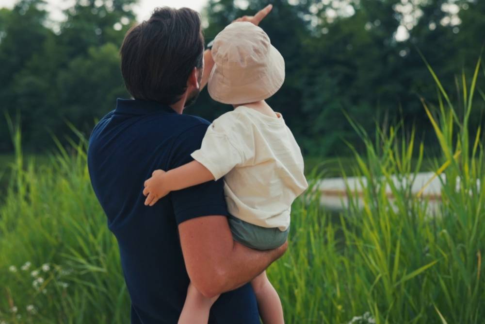 Vacation, summer, father holds his little son in arms, boy has a hat on head, man points to something with hand